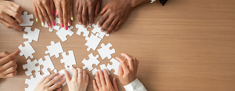 multi-ethnic hands reaching for puzzle pieces (top view)